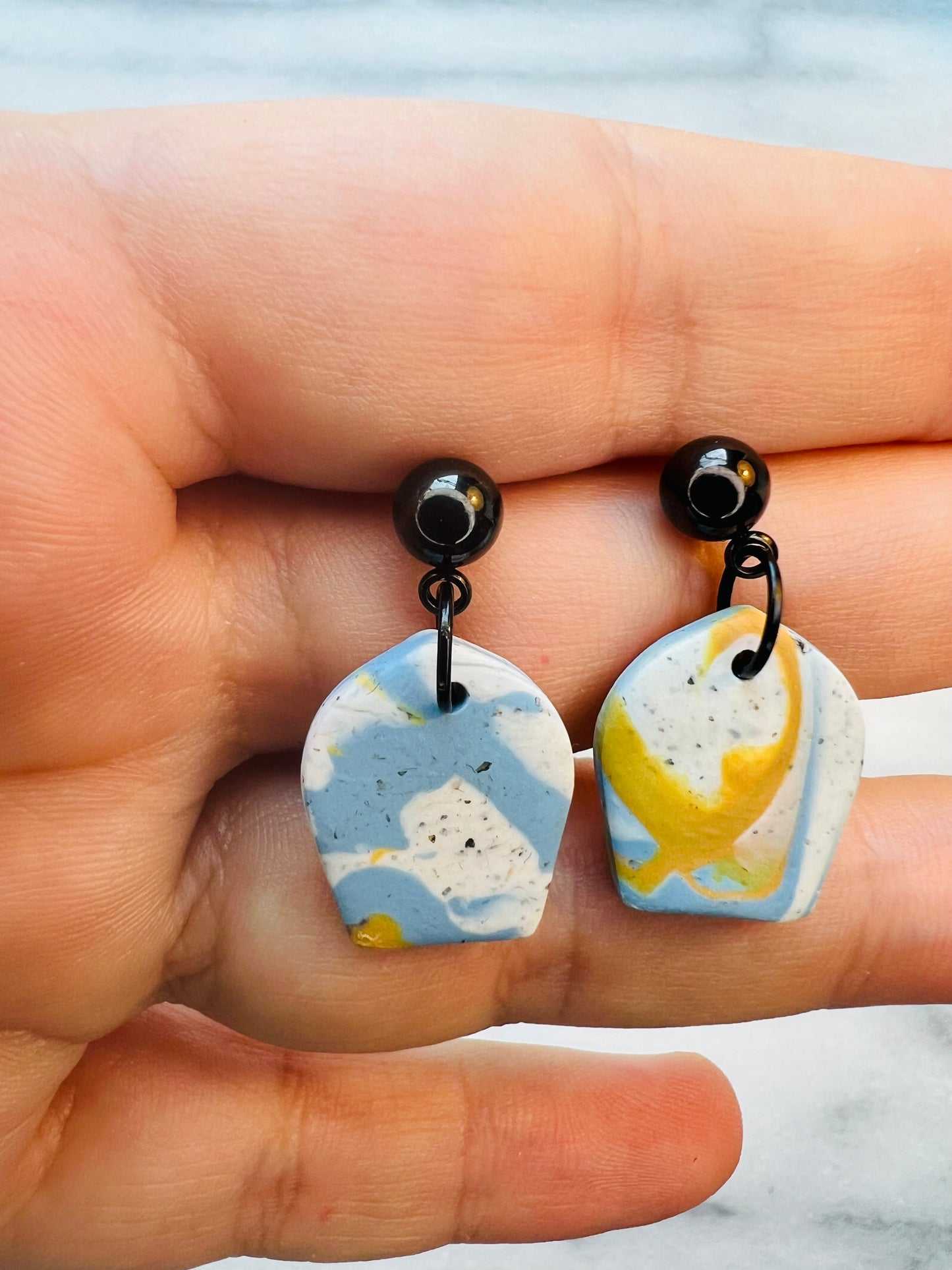 Marble-patterned earrings held between fingers with a blurred background
