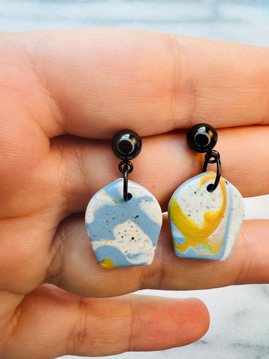 Marble-patterned earrings held between fingers with a blurred background